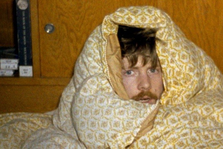 man wraped in a mustard coloured duvet with a moustache