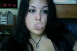 A woman with long dark hair and a leather necklace blows a bubble gum at her webcam