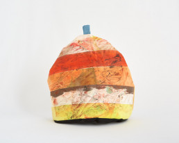 A painted yellow, white, orange and red striped handmade tea cosy