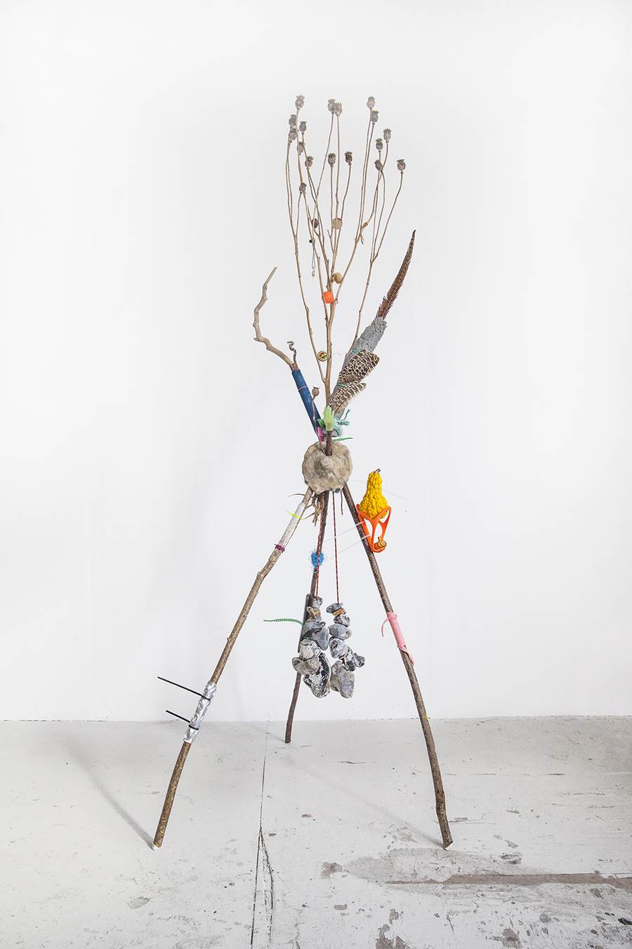 a tripod sculpture made with sticks, feathers and bits hang off the sticks on string