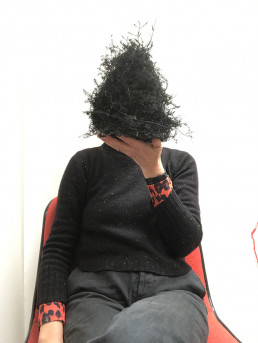 person sitting on a red chair wearing black holding a nest like bundle infront of their face