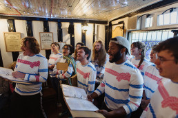 group of people singing wearing white, blue and pink striped tops