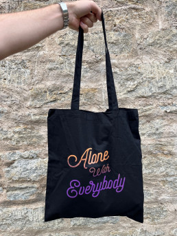 black tote with orange and purple text which read Alone with everybody in a script typeface