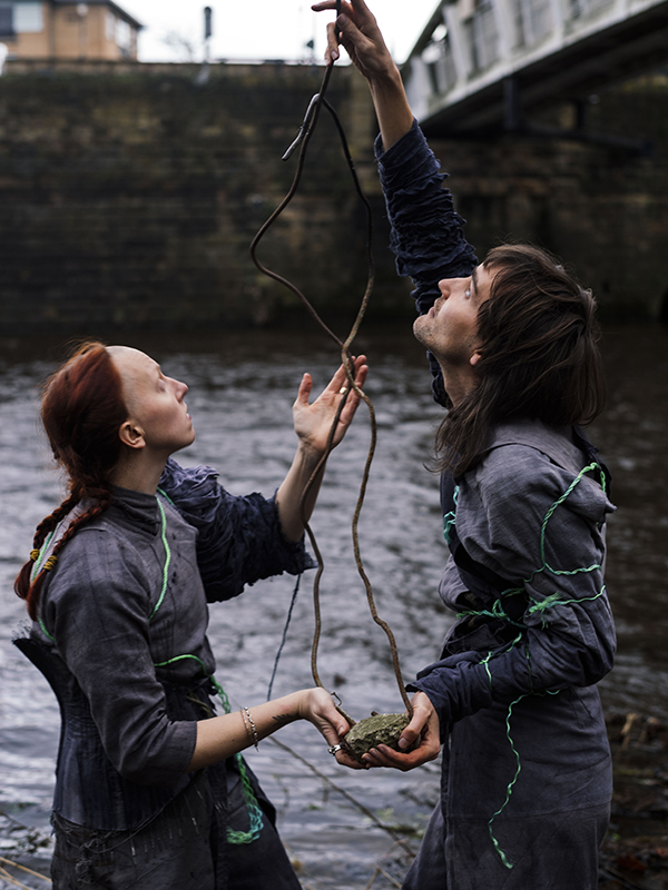 Two people standing near a river both holding a grey stone looking ball looking up to the sky