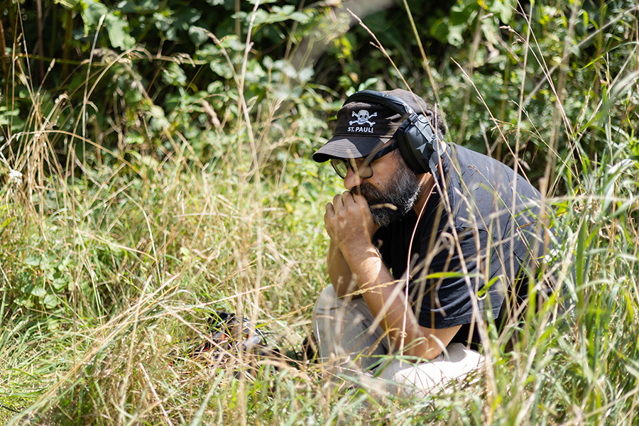 person sitting in long grass wearing a cap and headphones