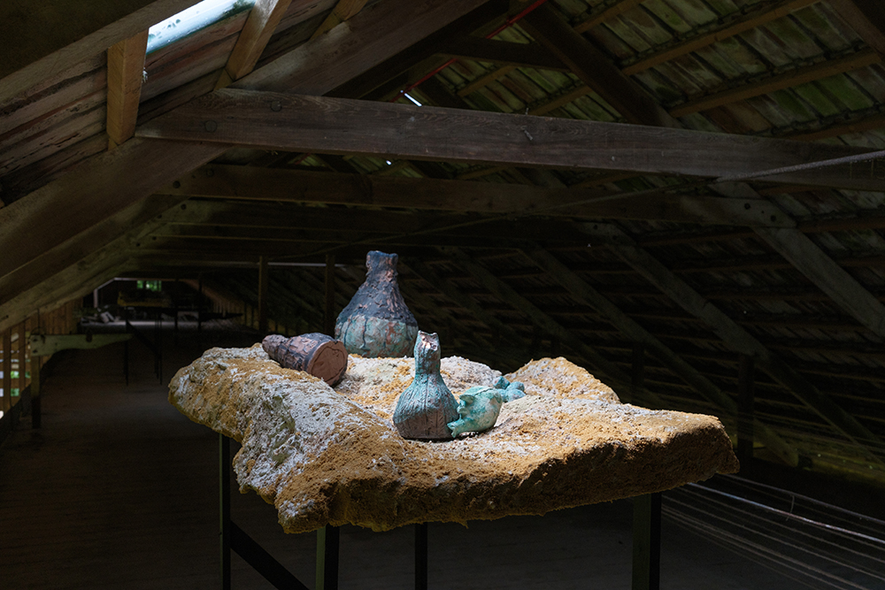 a landscape table which has tall dark legs, vases and pots nestled into the mountainous landscape. Highlighted by the skylight above.